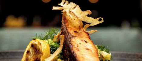 A plated dish with a grilled fish centerpiece, garnished with herbs and lemon slices.