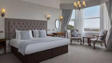 A spacious bedroom with a large bed, two armchairs, a small table, and a view of the city.