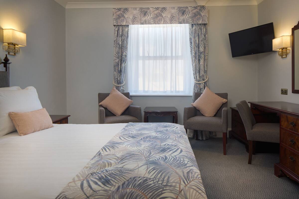 Habitación de hotel con una cama grande, dos sillones, una mesita, un televisor y un aparador.