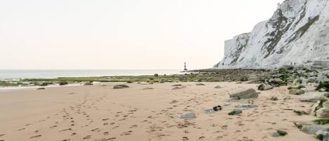 A beach with footprints, rocks, and a lighthouse in the distance.