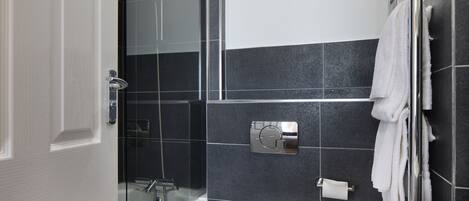 Un baño moderno con cabina de ducha de vidrio, inodoro blanco y un perchero para toallas.