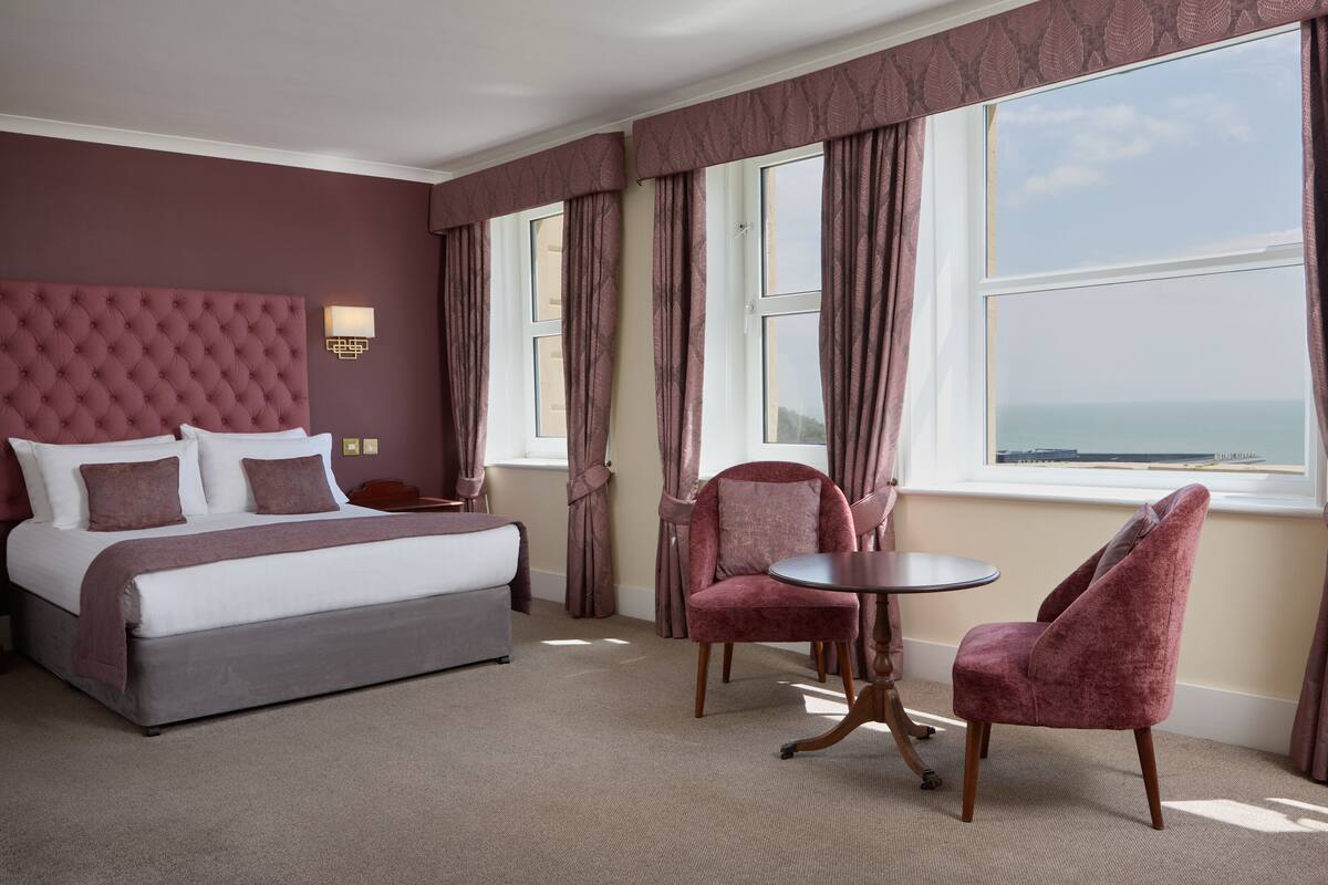 Habitación de hotel con una cama grande, dos sillones, una mesita y vista al mar.