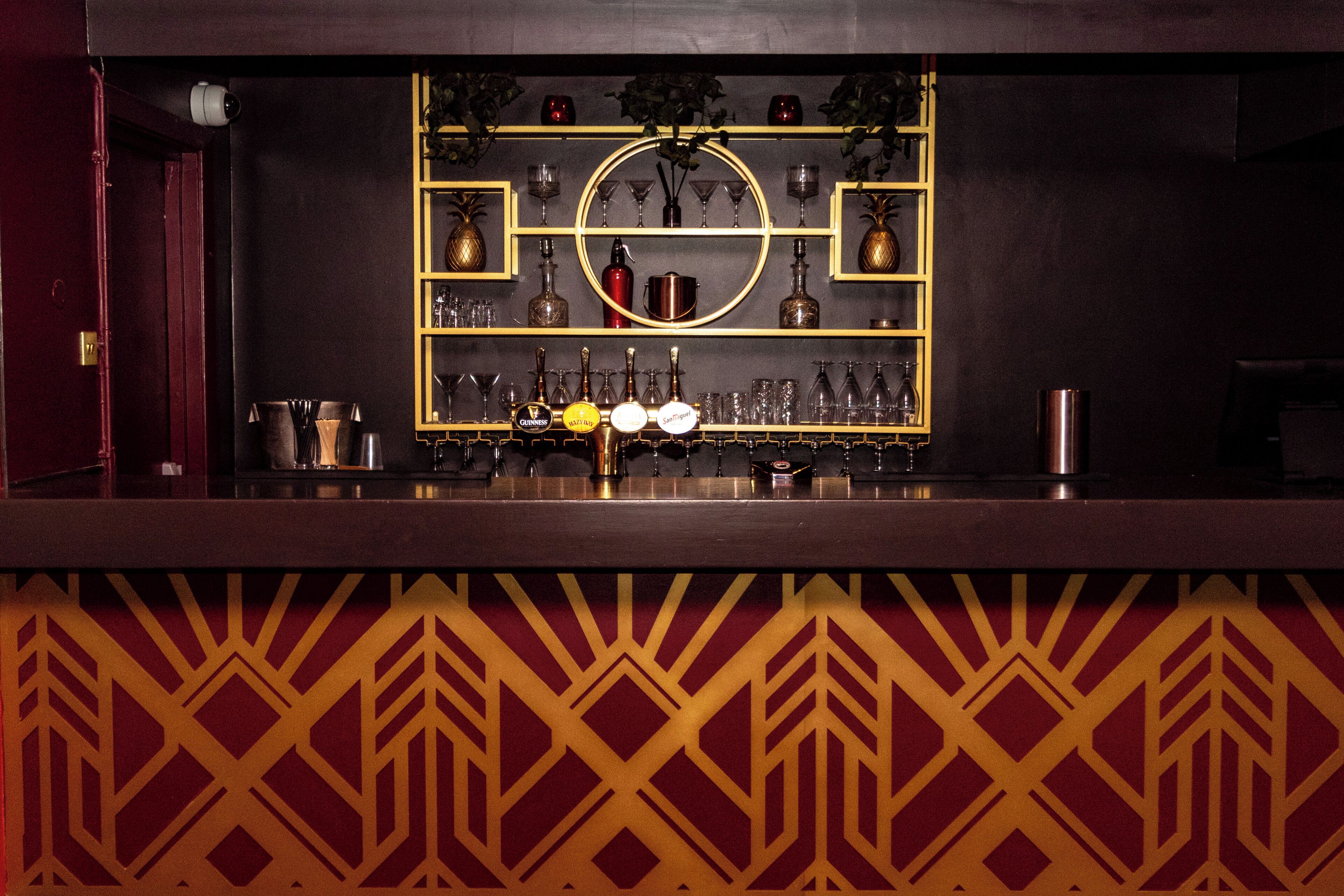 A bar area with shelves of bottles and glasses, a circular mirror, and a patterned wall.