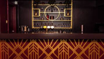 Un espace bar avec des étagères remplies de bouteilles et de verres, un grand miroir rond et un mur orné de motifs.