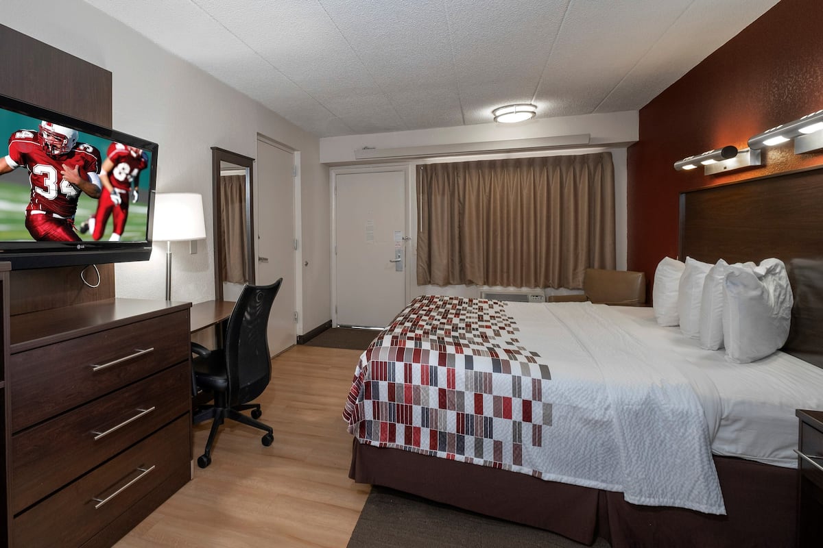 Hotellihuone, jossa on sänky, työpöytä tuolilla, televisio ja ovi.