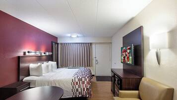 A hotel room with a bed, a desk, a chair, a television, and a door.