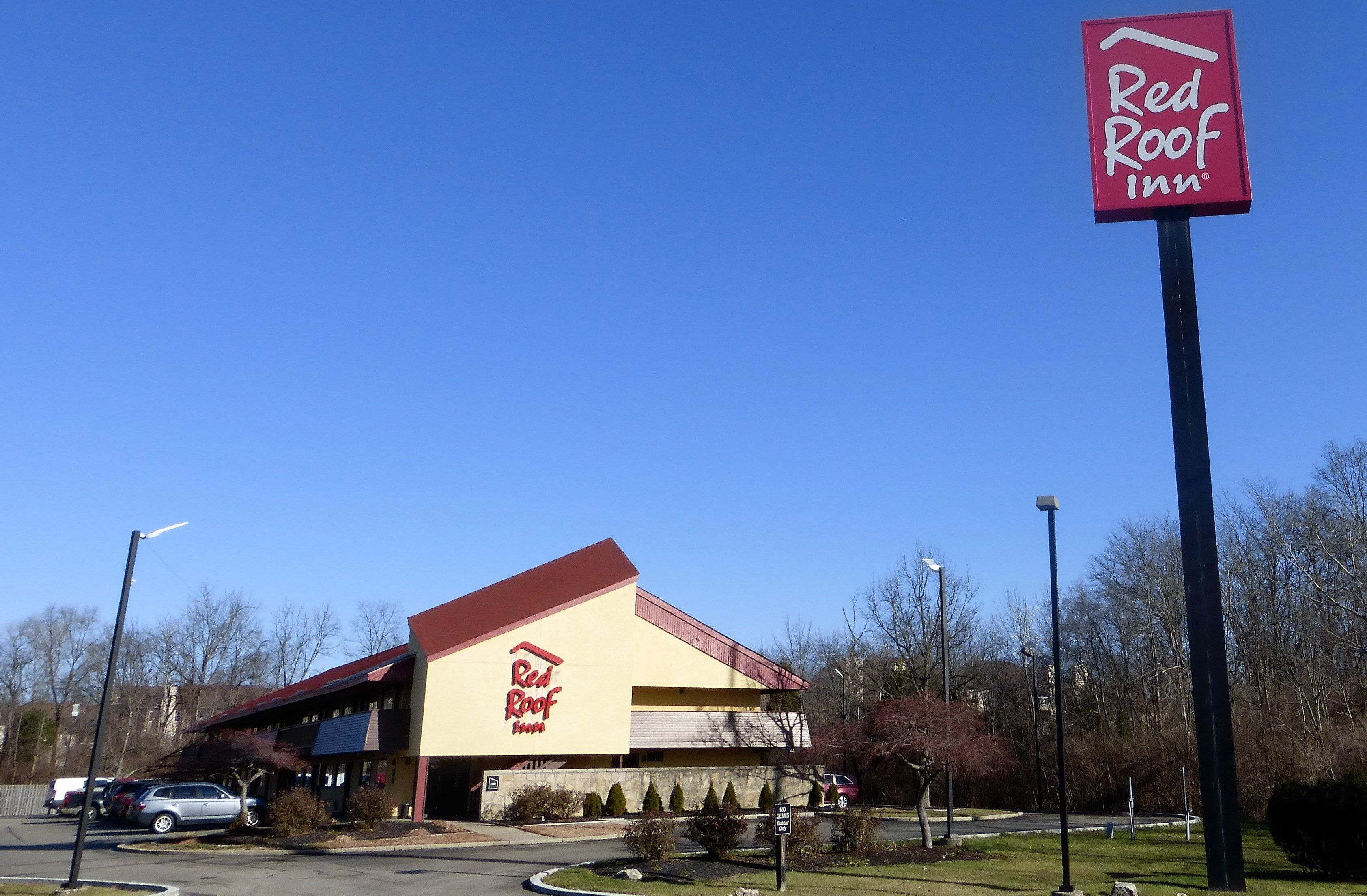 Un hotel Red Roof Inn con un llamativo letrero rojo y blanco, un estacionamiento y un cielo azul despejado.