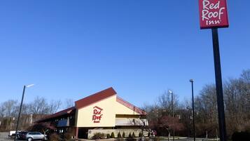 Un hotel Red Roof Inn con un llamativo letrero rojo y blanco, un estacionamiento y un cielo azul despejado.