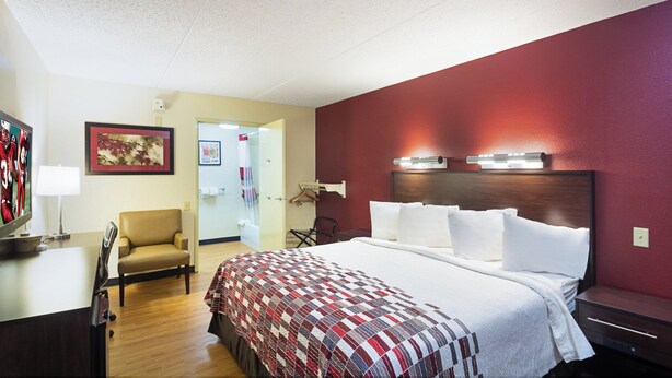 Ein Hotelzimmer mit einem Bett, einem Schreibtisch mit Lampe, einem Sessel und einem Fernseher.