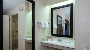 Ein Hotelbad mit einem großen Spiegel, einem Waschbecken, einem Handtuchhalter und einer Duschkabine.