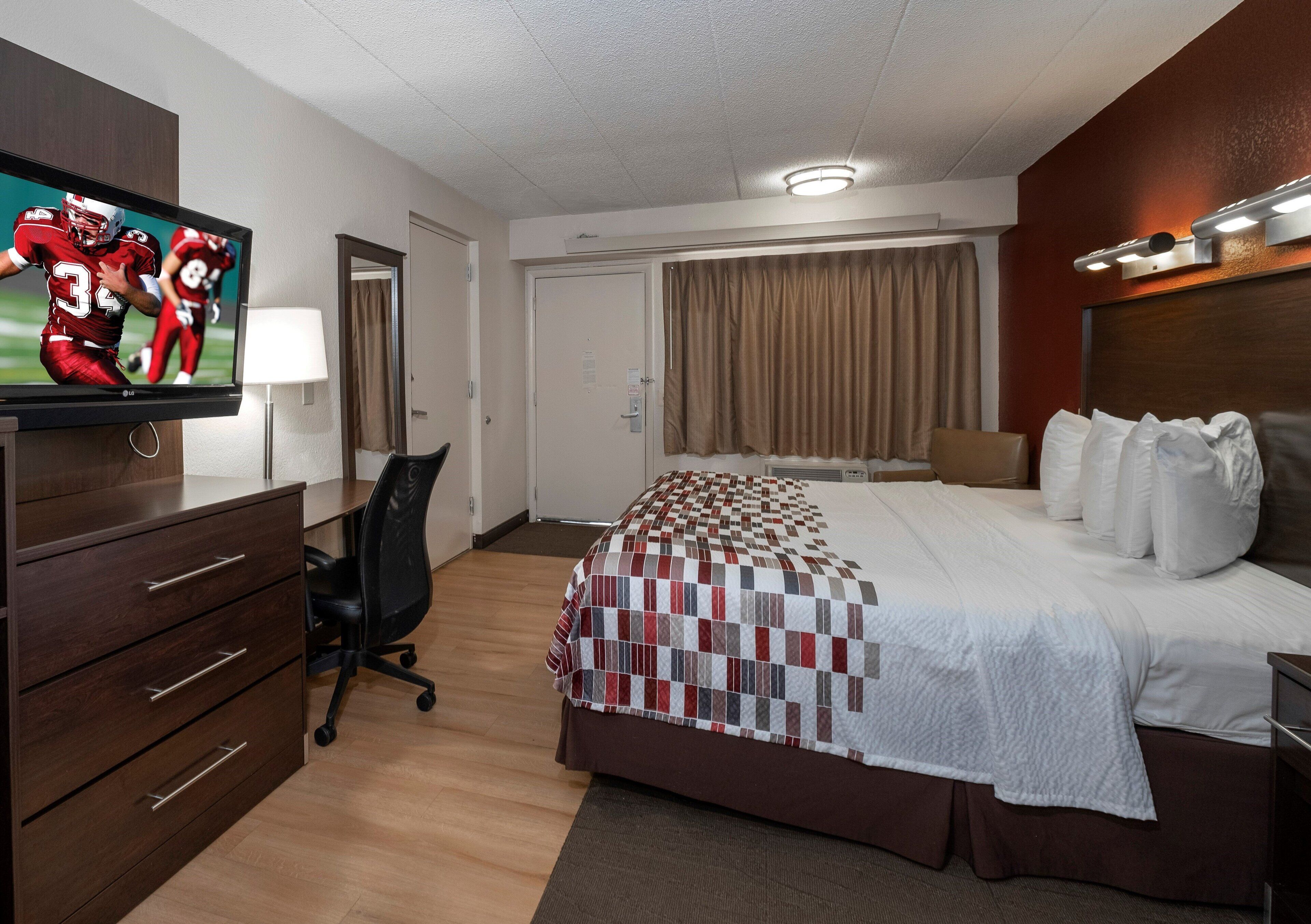 Ein Hotelzimmer mit einem Bett, einem Schreibtisch mit Stuhl, einem Fernseher und einer Tür.