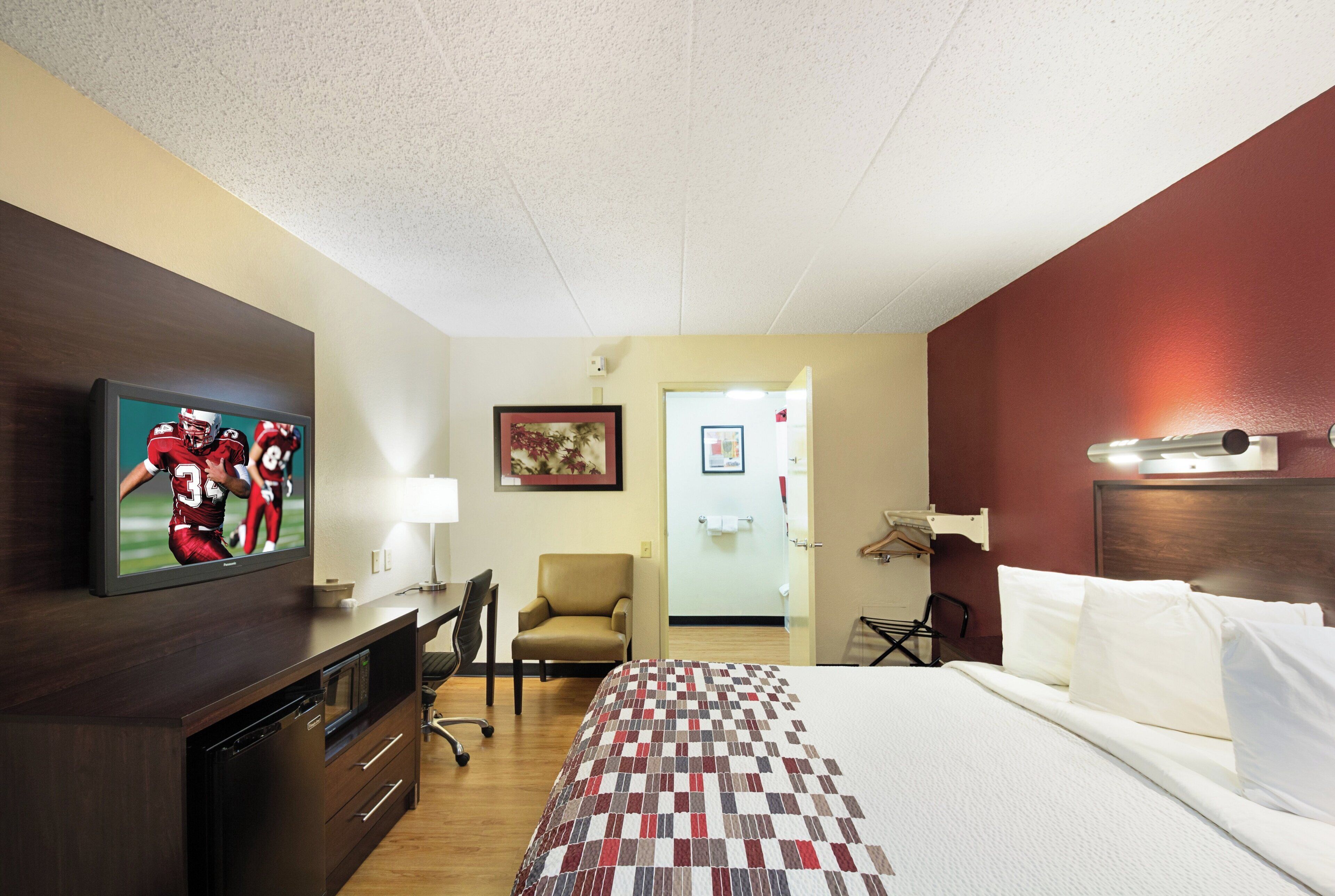 A hotel room with a bed, a desk, a chair, a television, and a door.
