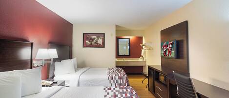 Habitación de hotel con dos camas, un escritorio, una silla, un televisor y un baño.