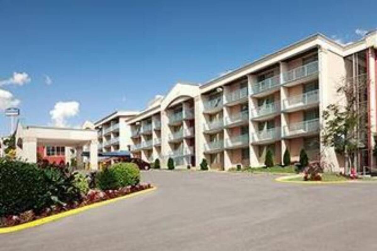 Un hotel a più piani con balconi, un parcheggio e un cielo sereno.