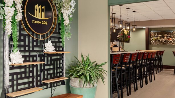 Un interior de restaurante con una pared decorativa, una planta en maceta y una larga mesa de comedor con sillas.