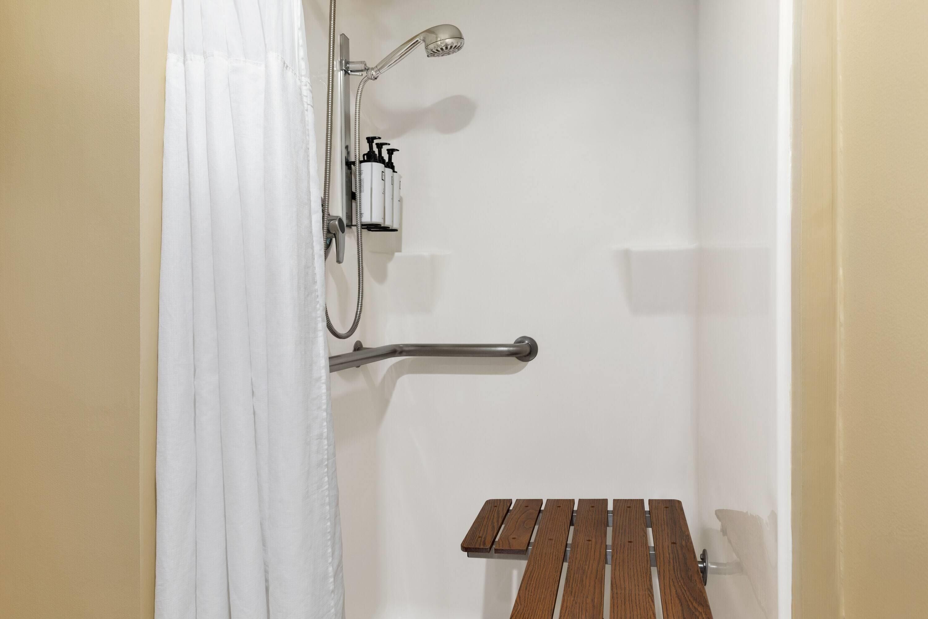 A shower area with a handheld showerhead, a grab bar, and a wooden bench.