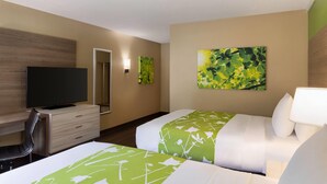 Habitación de hotel con dos camas, televisión, escritorio y obras de arte en las paredes.