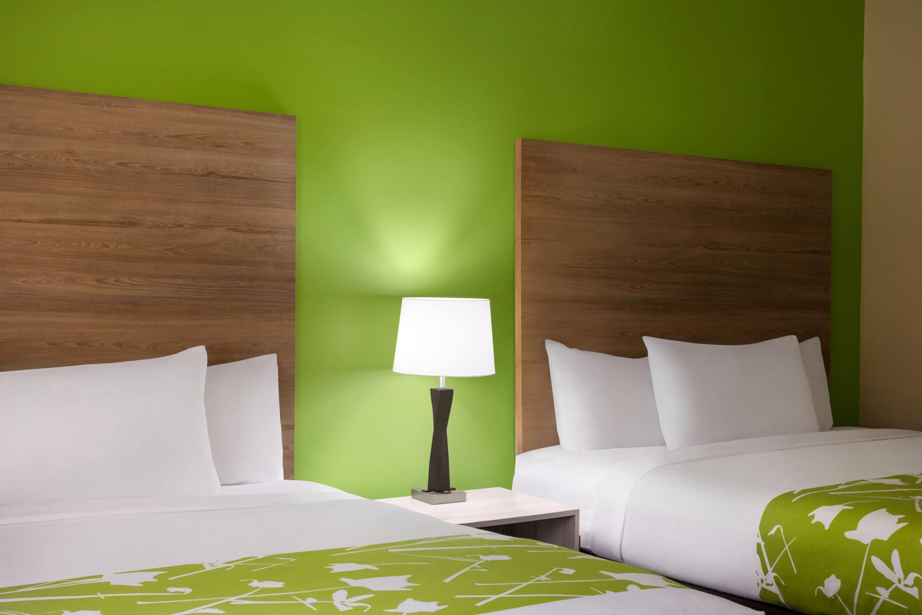 A hotel room with two beds, a nightstand with a lamp, and green walls.