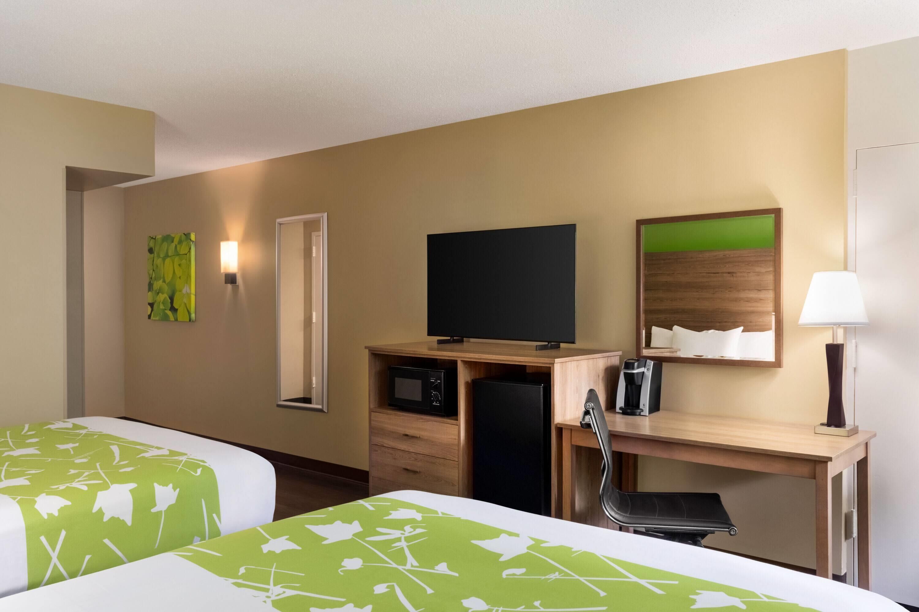 Habitación de hotel con dos camas, un escritorio, televisor, microondas, refrigerador, una silla y una lámpara.