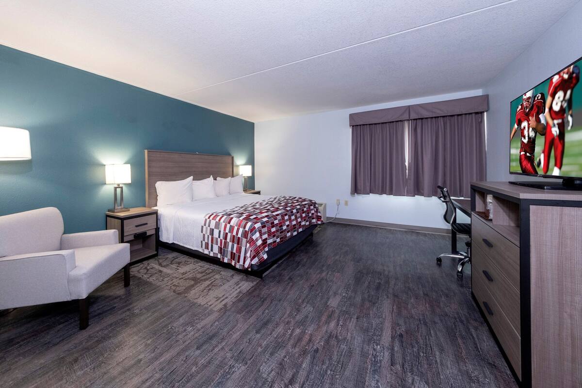 Ett hotellrum med en säng, ett skrivbord, en stol, en tv och ett fönster med gardiner.