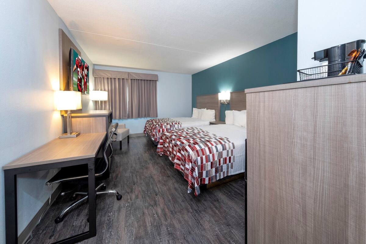 Ett hotellrum med ett skrivbord, två sängar, en sänggavel och ett fönster med gardiner.
