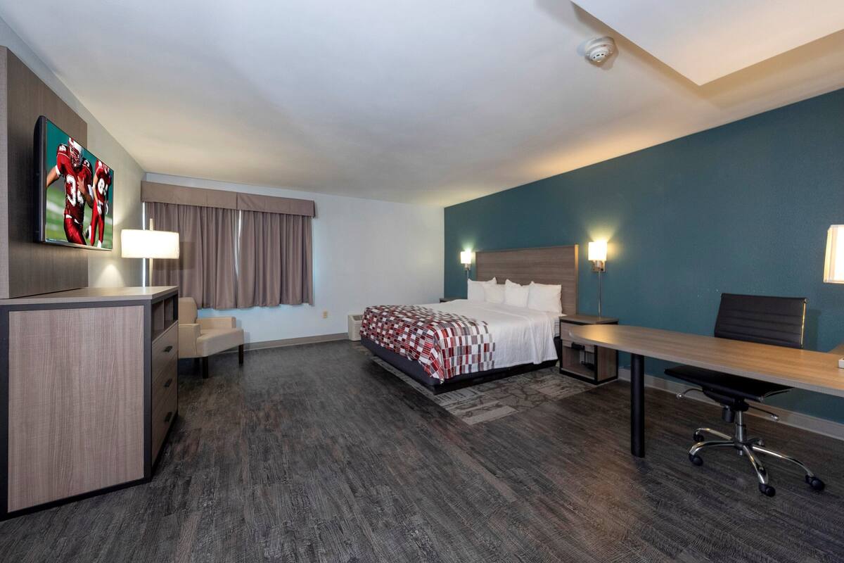 Ett hotellrum med en säng, ett skrivbord, en stol och en tv på väggen.