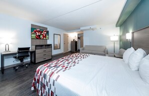 Een hotelkamer met een groot bed, een bureau met een stoel, een aan de muur bevestigde televisie, een dressoir en een bank.