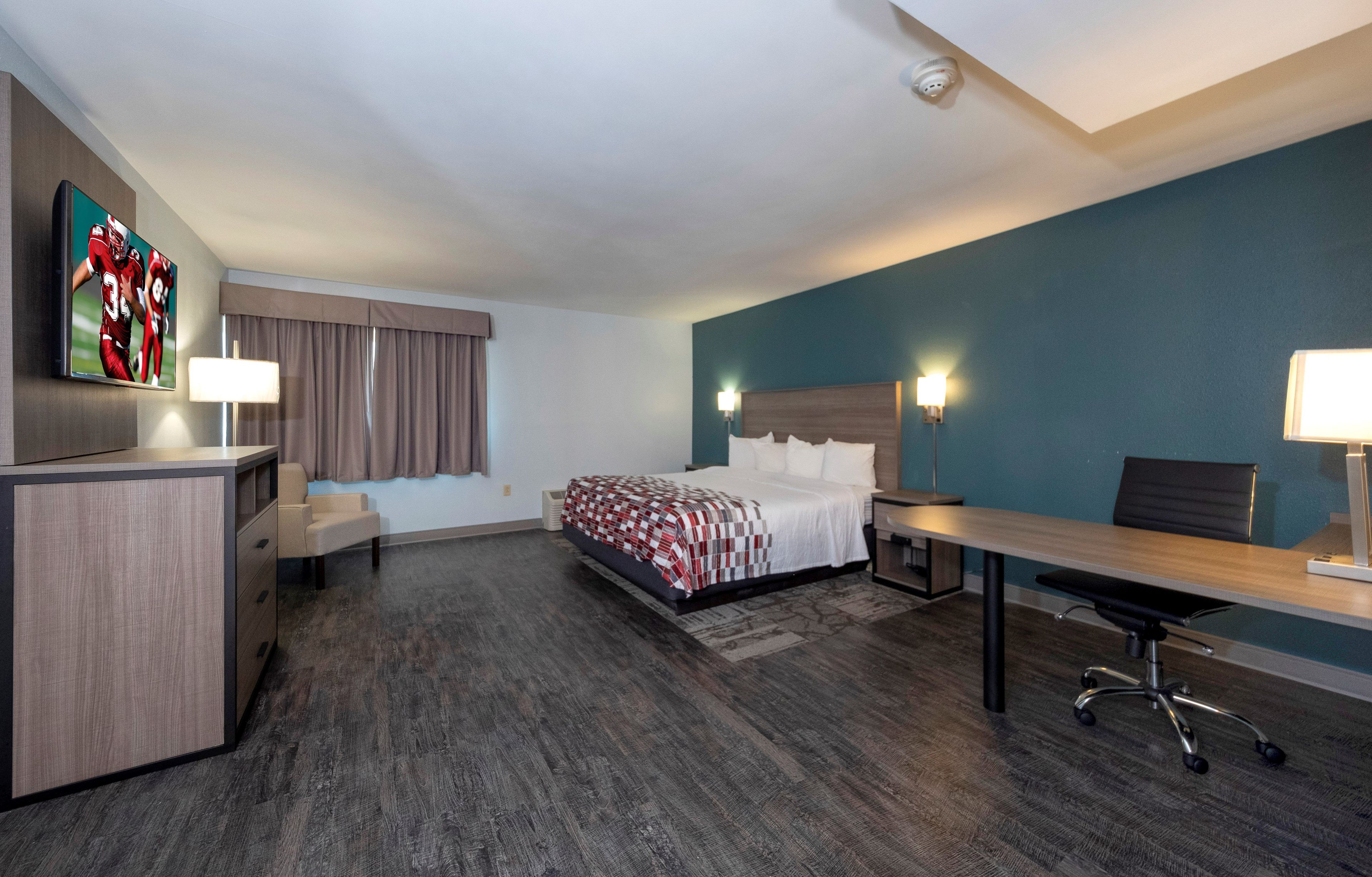 A hotel room with a bed, desk, chair, and a TV mounted on the wall.