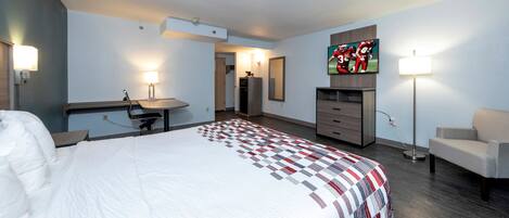 A hotel room with a bed, a desk, a chair, a TV, and a lamp.