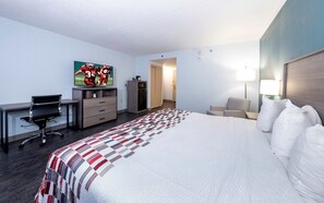 Ein Hotelzimmer mit Bett, Schreibtisch mit Stuhl, Fernseher, Kleiderschrank und Nachttisch mit Lampe.