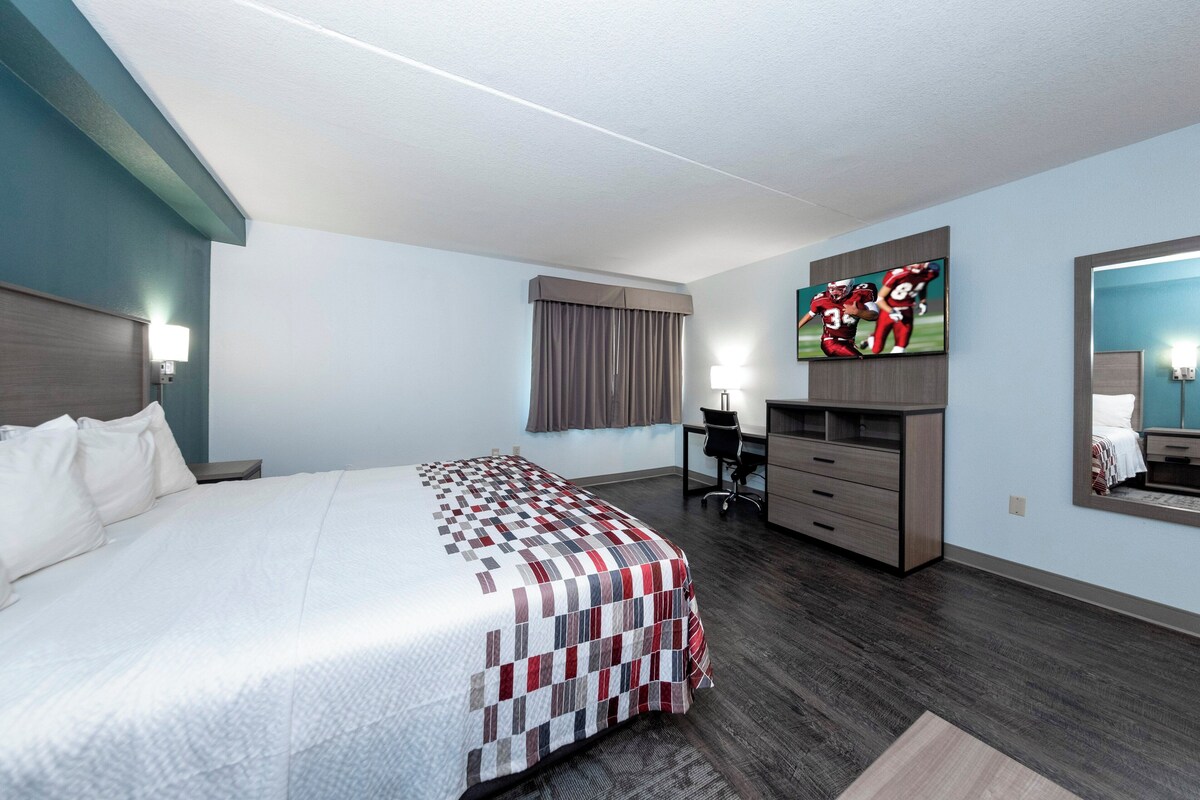Une chambre d’hôtel avec un grand lit, un bureau, une chaise, une télévision et un miroir.