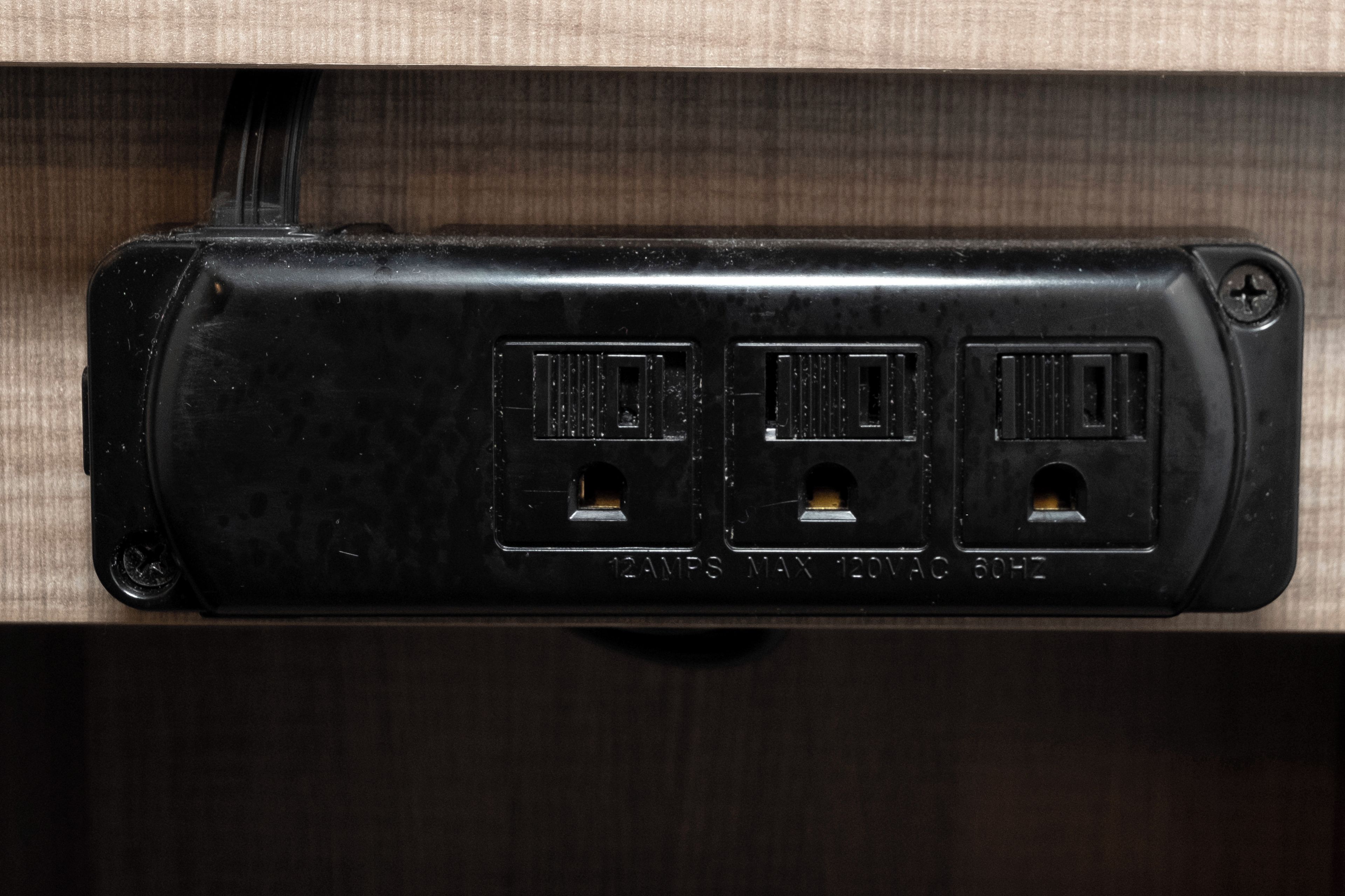 A black electrical outlet with three sockets, labeled '12AMP MAX 120VAC 60HZ'.