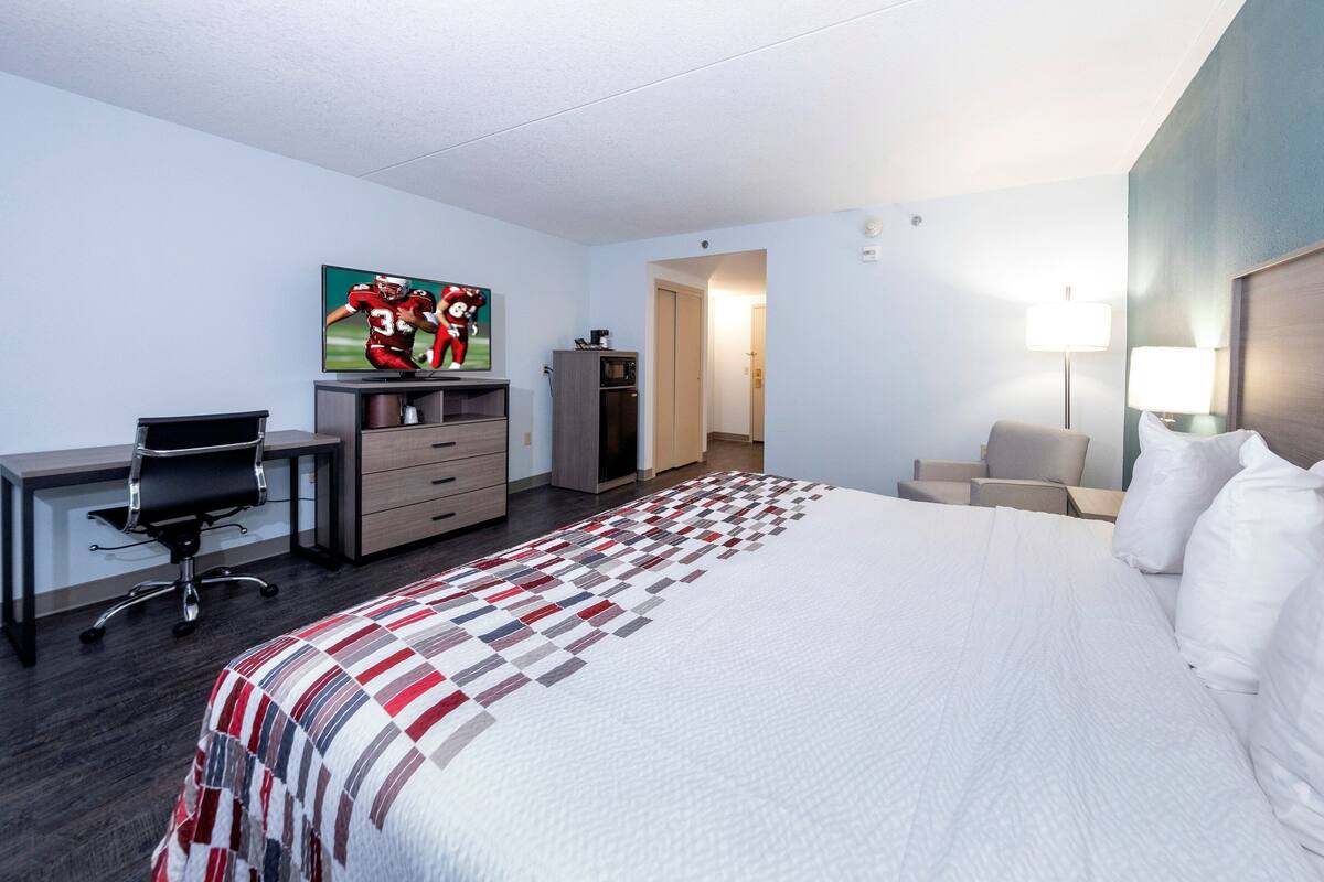 Hotelkamer met een bed, een bureau met stoel, een televisie, een kledingkast en een nachtkastje met lamp.