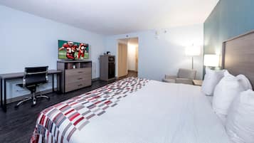 A hotel room with a bed, desk, chair, television, wardrobe, and a painting on the wall.