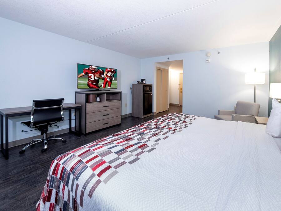 A hotel room with a bed, desk, chair, television, wardrobe, and a painting on the wall.