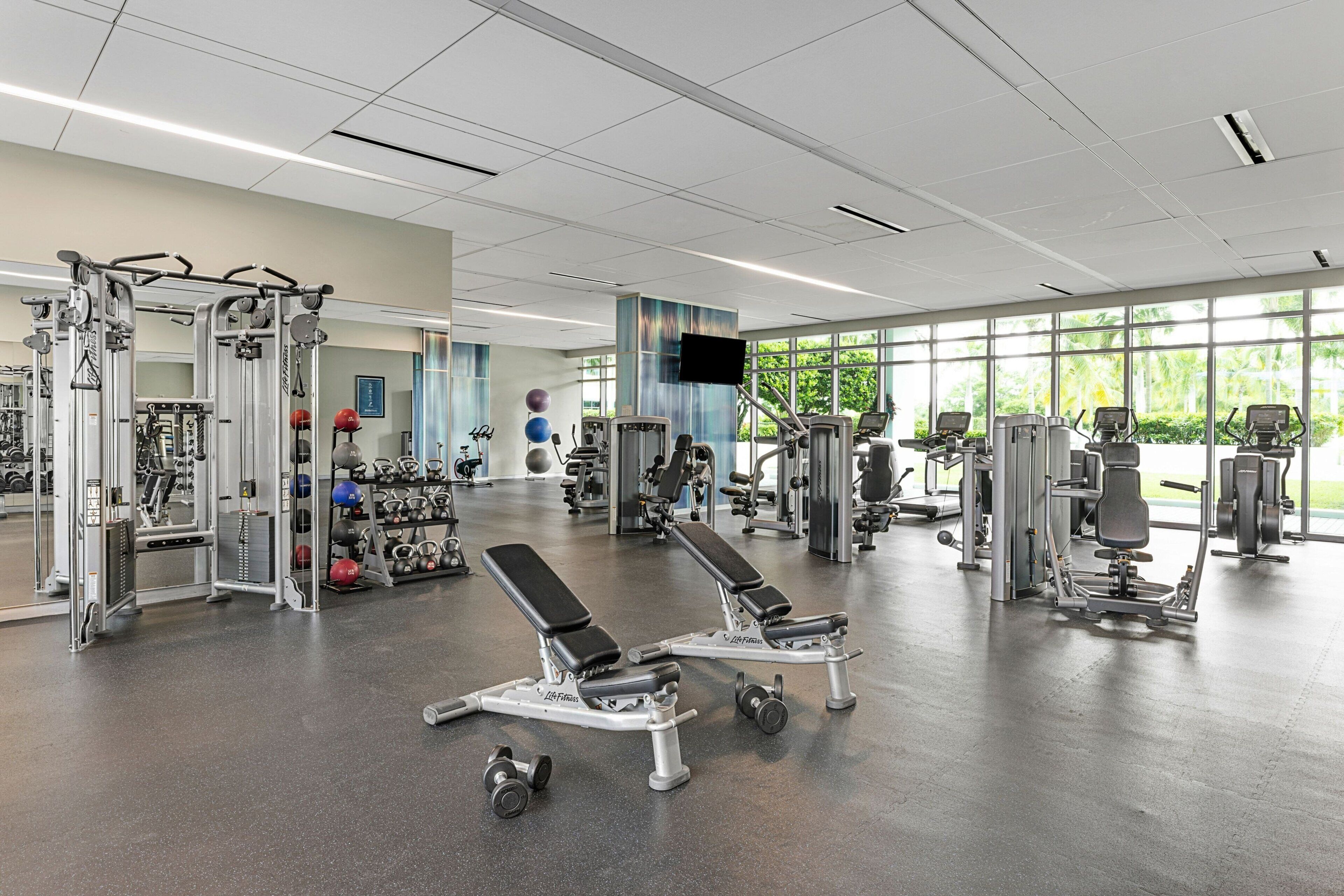 Ein geräumiges Fitnessstudio mit unterschiedlichen Trainingsgeräten, großen Fenstern und einem sauberen, modernen Design.