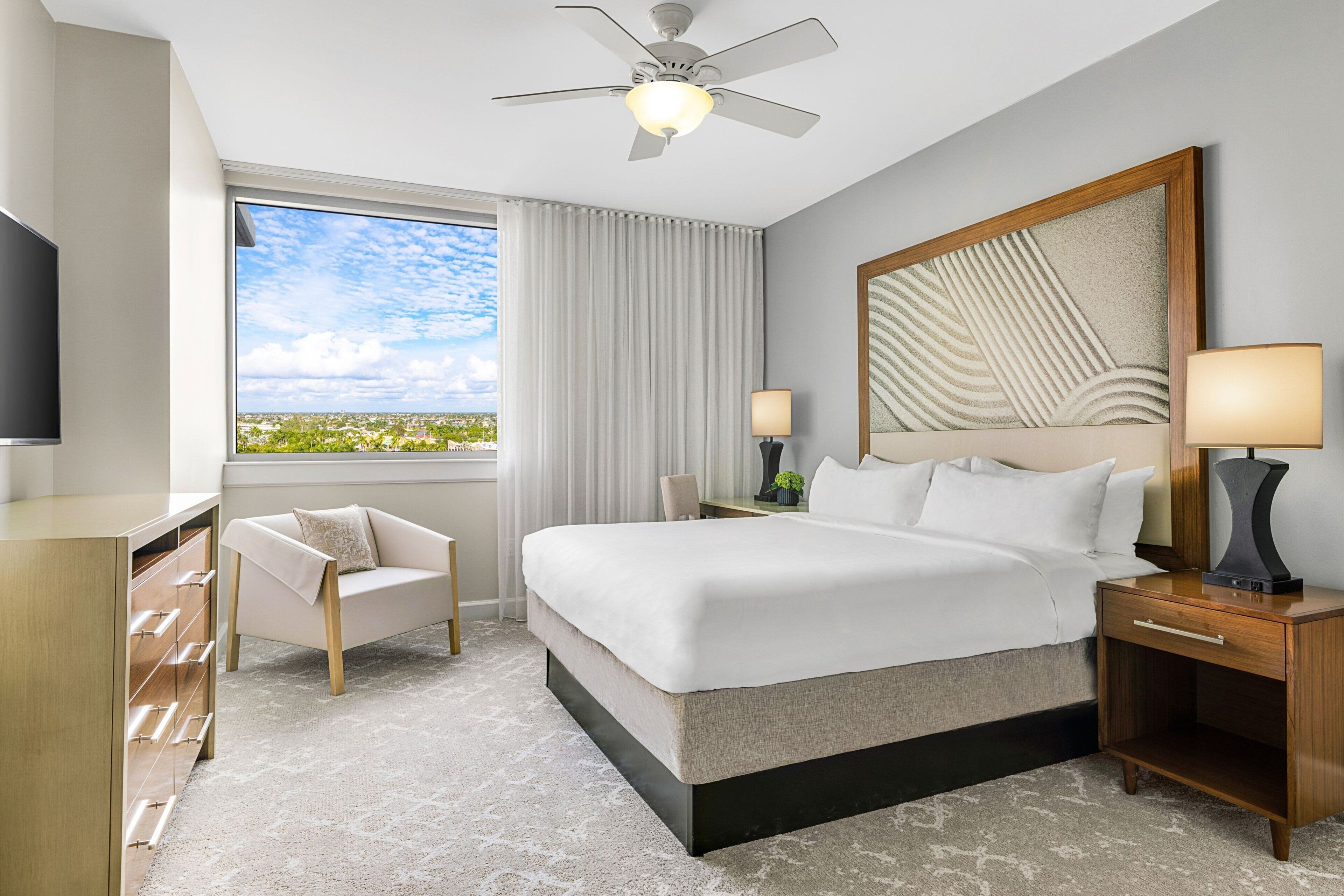Une chambre d’hôtel avec un grand lit, une télévision, un bureau, une chaise et une vue sur la ville.