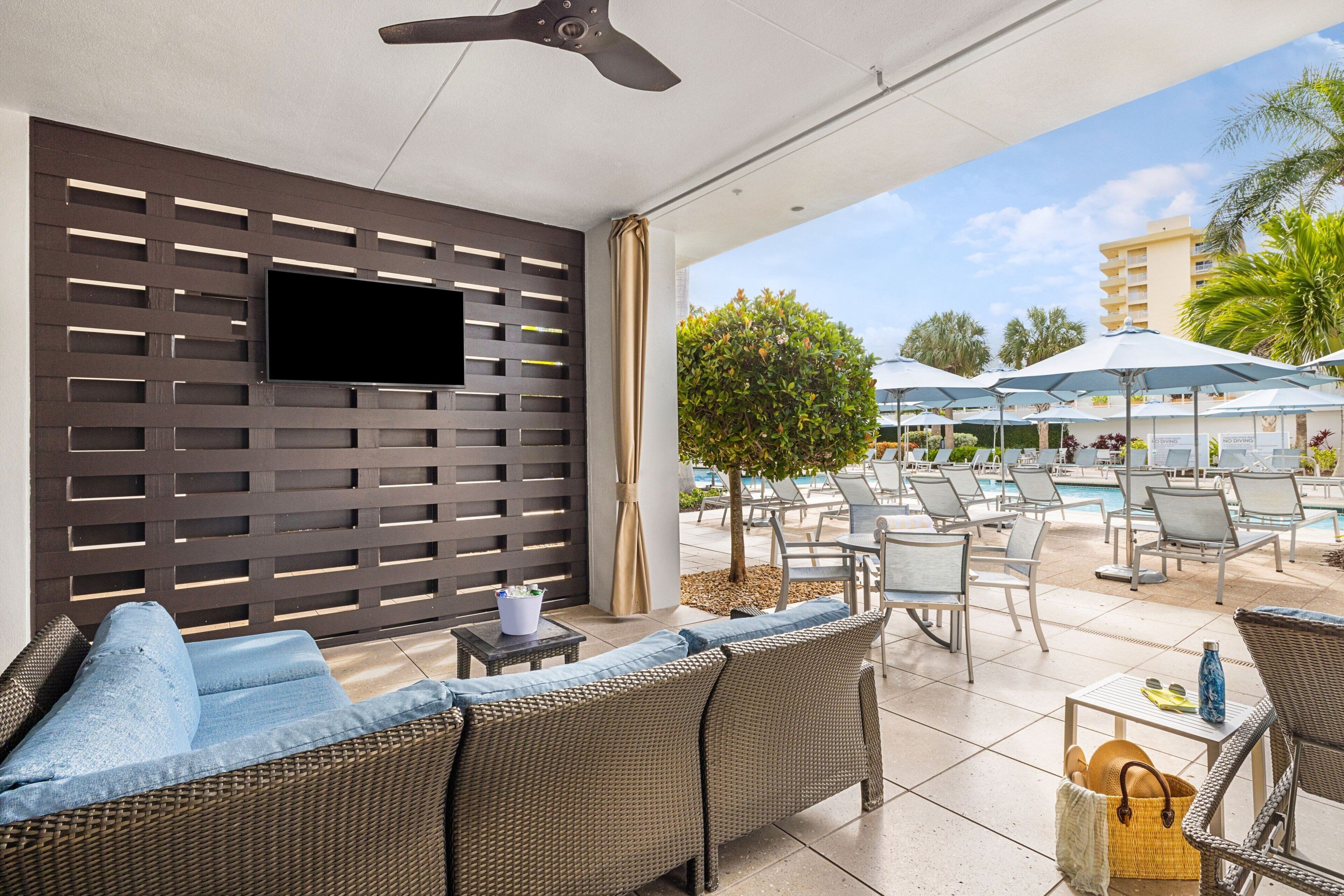 A modern outdoor lounge area with wicker furniture, a flat-screen TV, and umbrellas.
