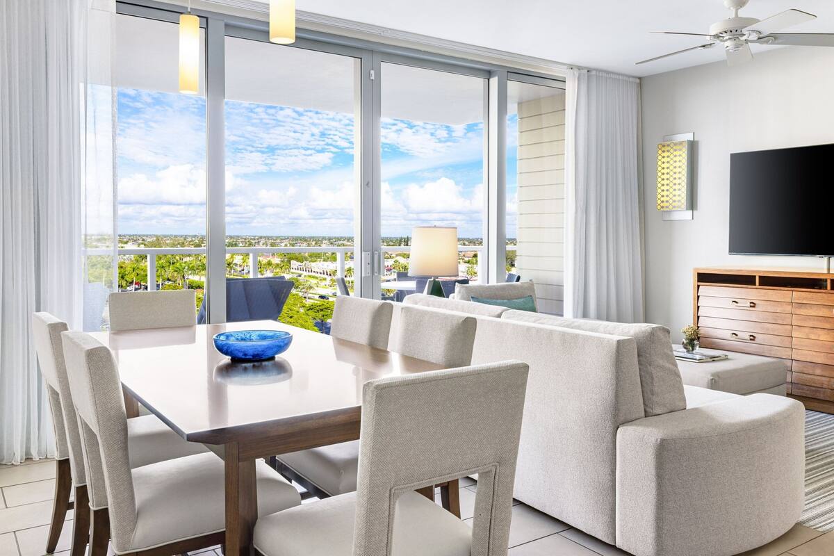A modern living room with a dining area, a sofa, a TV, and a balcony with a view.