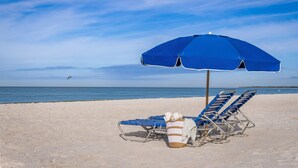 Ein Strand mit zwei blauen Liegestühlen und einem blauen Sonnenschirm.