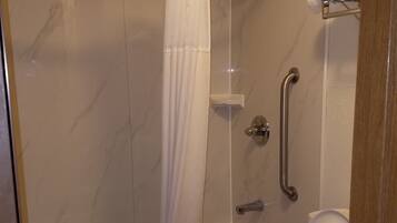 A bathroom with a glass-enclosed shower, a white toilet, and a grab bar for safety.