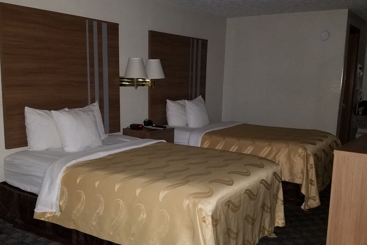 A hotel room with two beds, a nightstand with a lamp, and a wooden headboard.