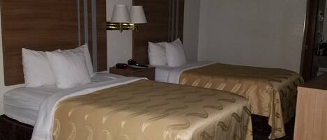 Una habitación de hotel con dos camas, una mesita de noche con lámpara y cabecera de madera.