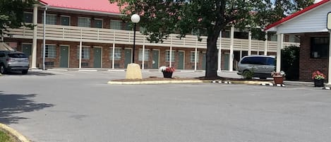 Un estacionamiento con un edificio de techo rojo y paredes de ladrillo. Hay árboles y plantas en macetas alrededor del área.