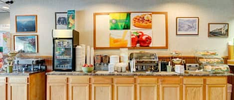 Ein Frühstücksbuffet mit einer Kaffeemaschine, einem Kühlschrank und verschiedenen Speisen.