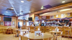 A restaurant with wooden interiors, multiple tables and chairs, a bar area, and a television screen.