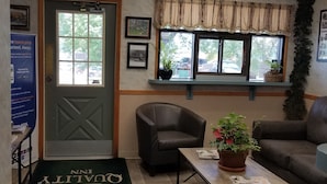 A reception area with a reception desk, a leather armchair, a coffee table with a plant, a couch, and a door with a window view.