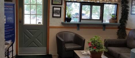 A reception area with a reception desk, a leather armchair, a coffee table with a plant, a couch, and a door with a window view.