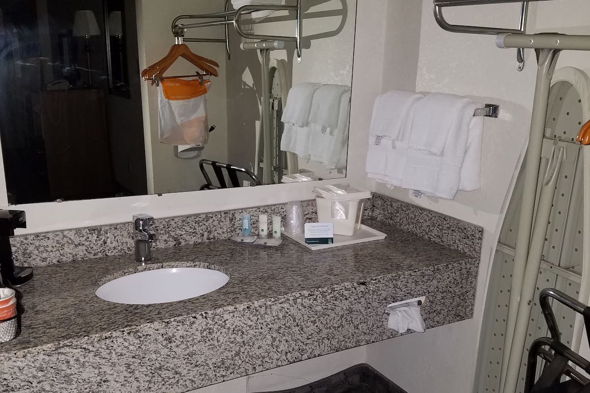A bathroom with a granite countertop, a sink, a mirror, and a towel rack.