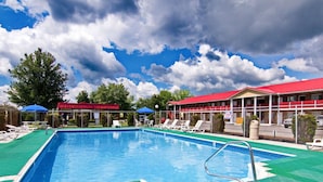 A swimming pool with a green deck, lounge chairs, and a red-roofed building in the background.
